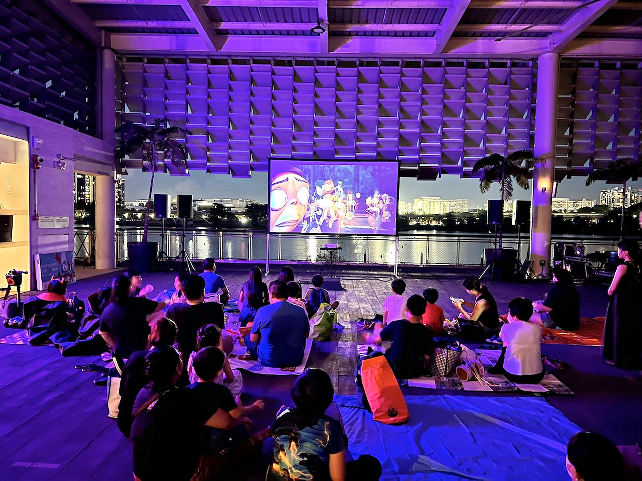 Movie Screening: 6 Easy Ways to Plan Better Seating 2 Guests seated on mats facing a waterfront movie screen